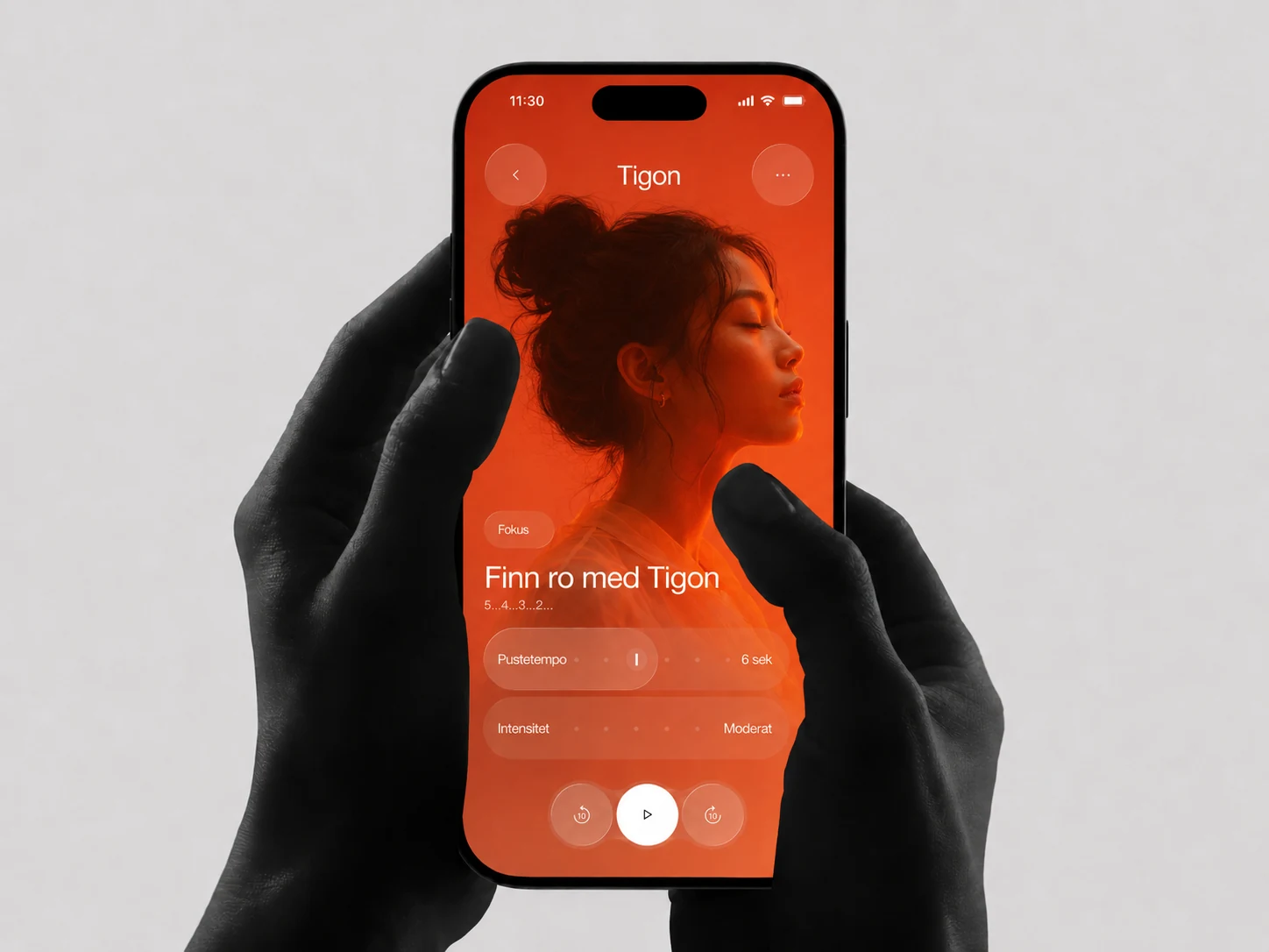 En hånd holder en smarttelefon med en oransje Tigon-app for meditasjon, fokus og pustetempo.